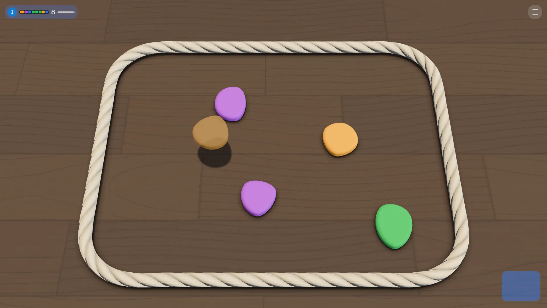 A Dropstone board: flat stones in purple, orange and green inside a loop of white rope on a wooden table, and a translucent brown stone hanging over its shadow, about to be dropped.